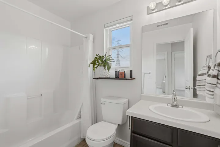 Full bathroom featuring a white tub and shower combination, a single vanity with a white countertop and dark wood-finish cabinetry, a white toilet, and a large wall-mounted mirror