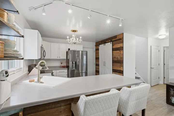 Kitchen featuring a large island with a composite countertop, a white single-basin sink with a gooseneck faucet, white shaker-style cabinetry, and stainless steel appliances