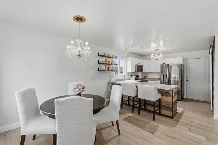 Kitchen and dining area featuring light-tone wood-finish flooring, white cabinetry, stainless steel appliances, a wood-paneled kitchen island with a light-toned countertop, and a crystal chandelier