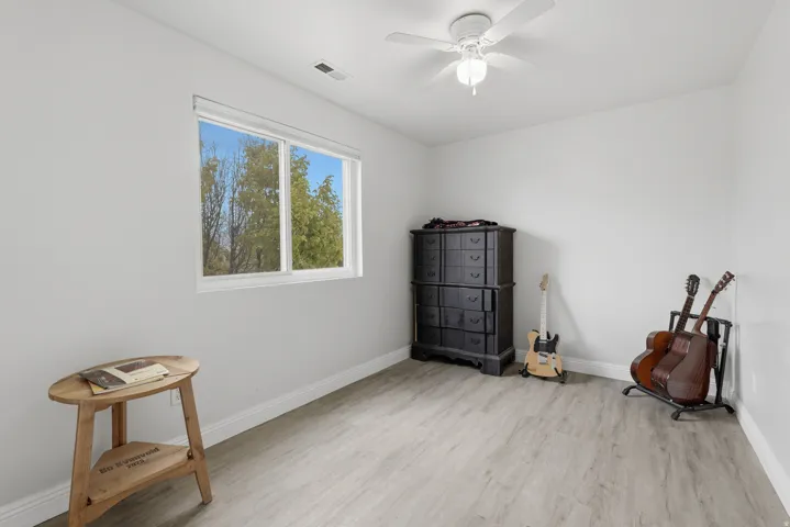 Bright room featuring wood-finish flooring, a white ceiling fan with integrated lighting, and a large window