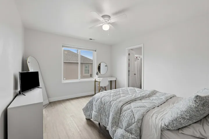 Bright bedroom featuring wood-finish flooring, a white ceiling fan with integrated lighting, and a window with blinds