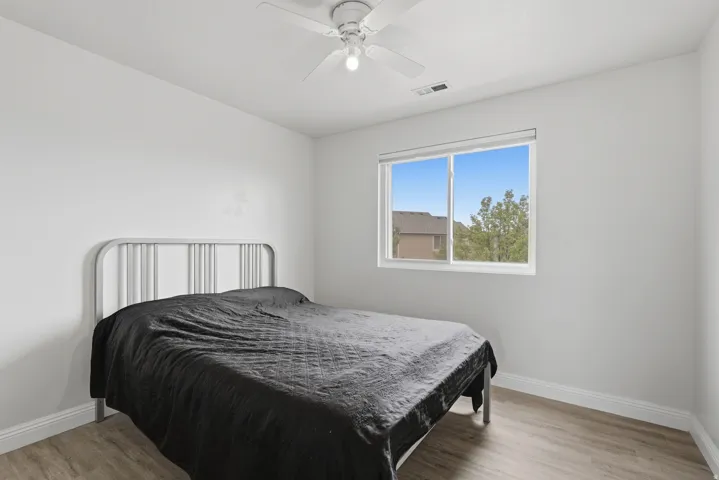 Bright room with light wood-finish flooring, a white ceiling fan with integrated lighting, and a window providing natural illumination