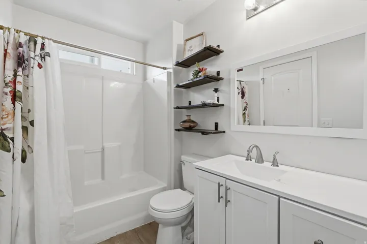 Bathroom featuring a white vanity with integrated sink, brushed nickel faucet, a frameless mirror, and a white shower/tub combination with a transom window