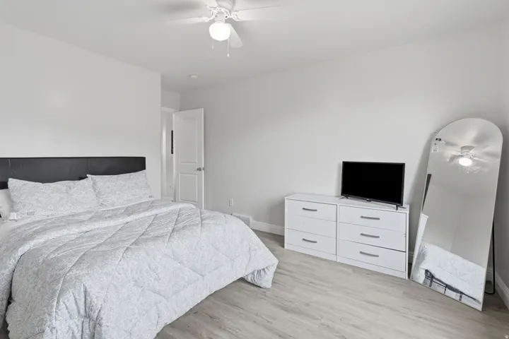 Bright room featuring light wood-finish flooring, a white ceiling fan with integrated lighting, and crisp white walls