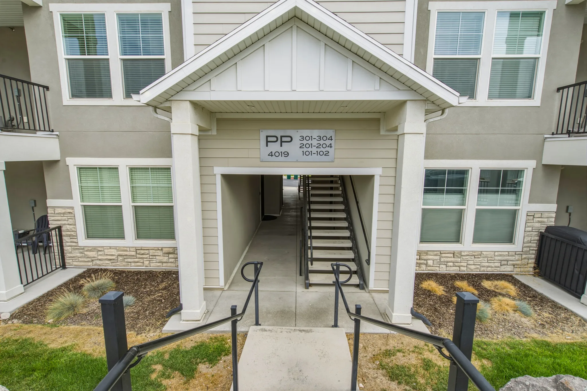 Multi-story building entrance with a gabled portico, stone veneer accents, and exterior siding