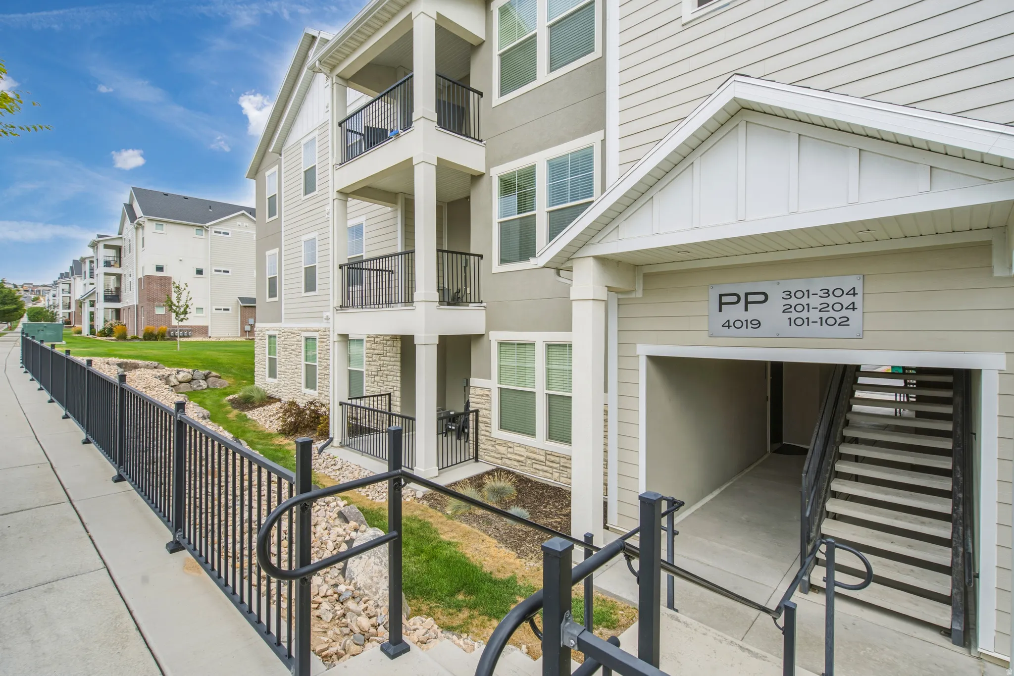Multi-story apartment building exterior featuring light-colored siding, stone accents, and black railings