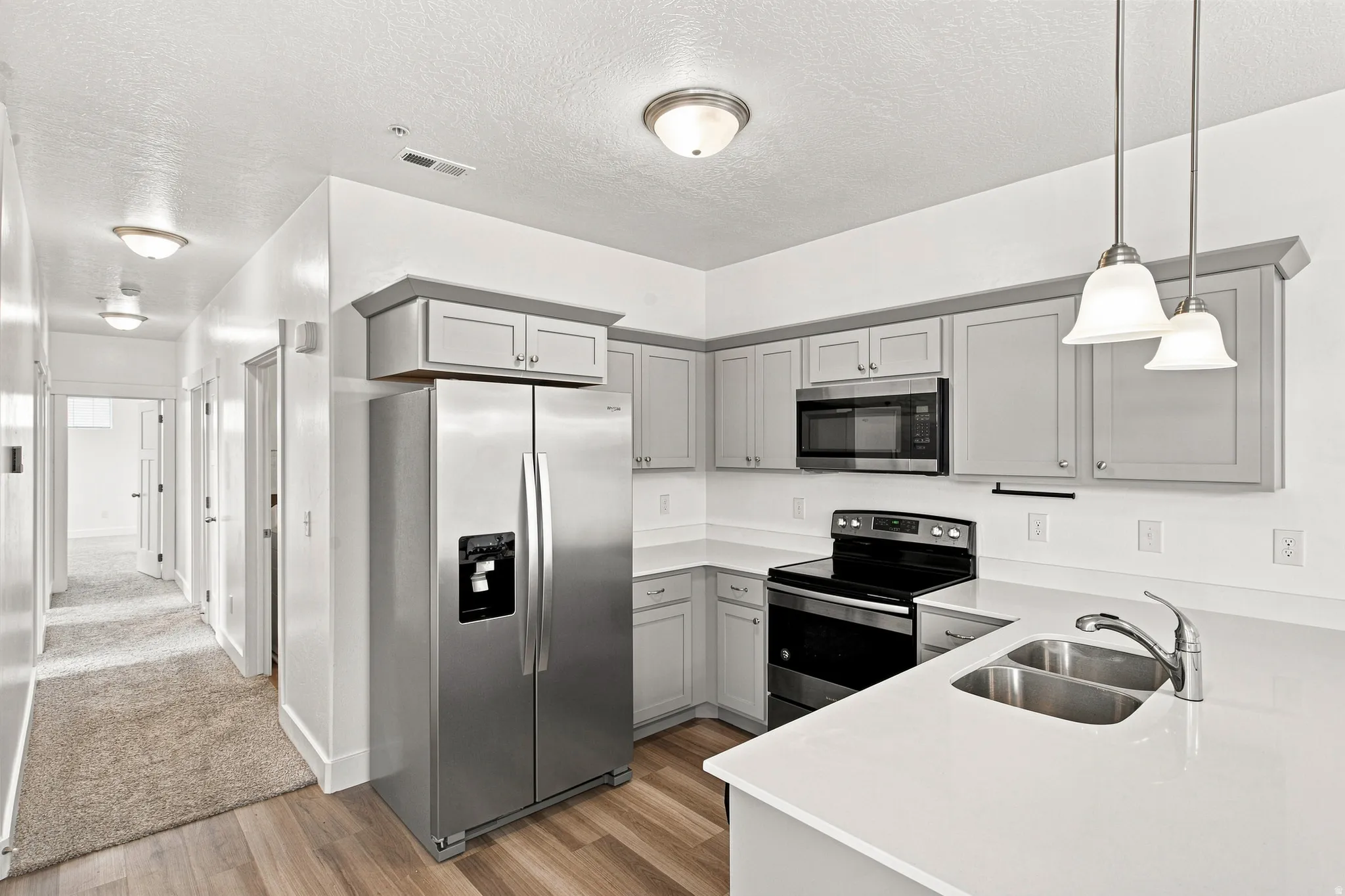 Kitchen featuring light gray cabinetry, stainless steel appliances, light-toned countertops, a double basin sink, and wood-finish flooring