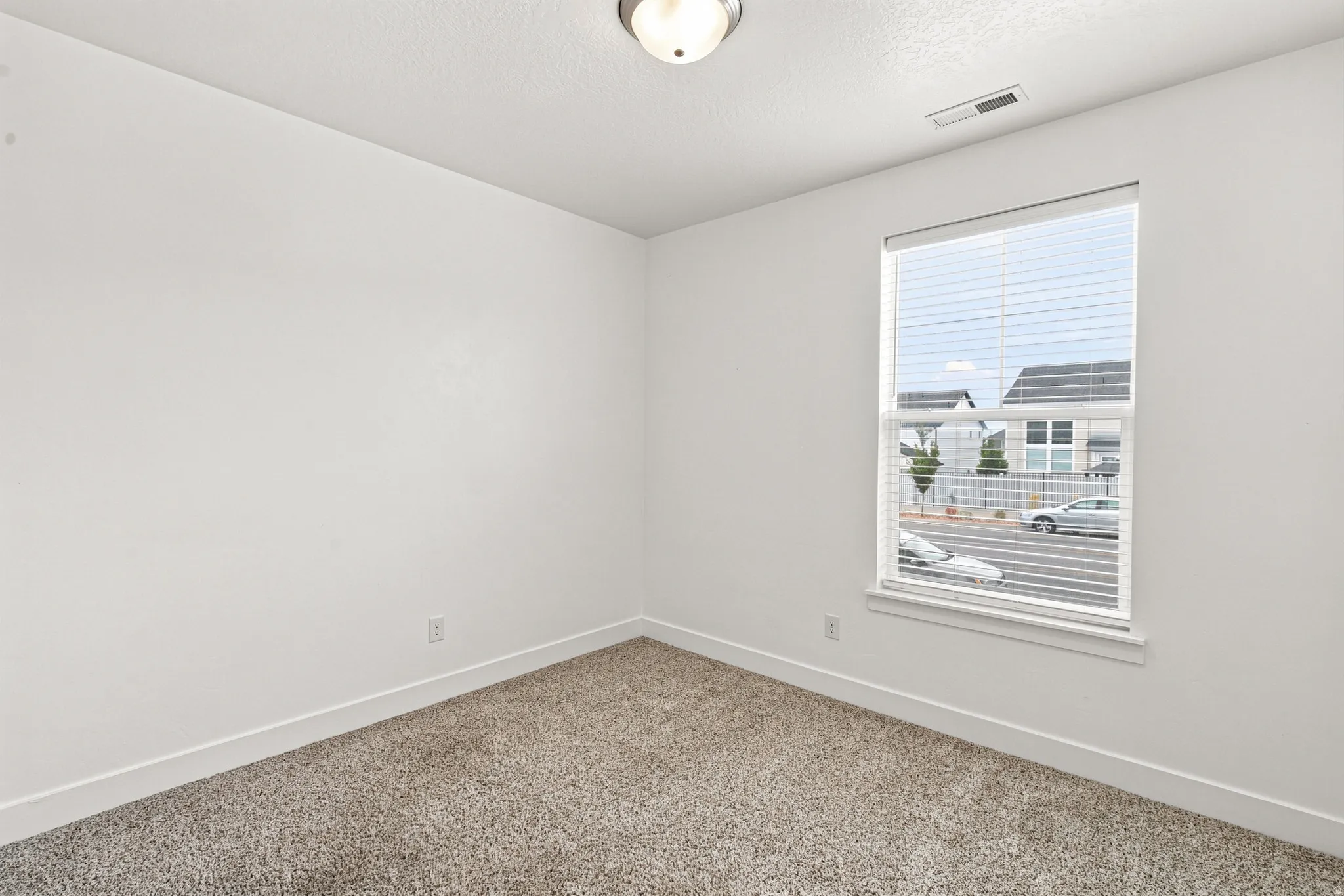 Carpeted room featuring a single window with blinds, white walls, and a flush-mount ceiling light fixture
