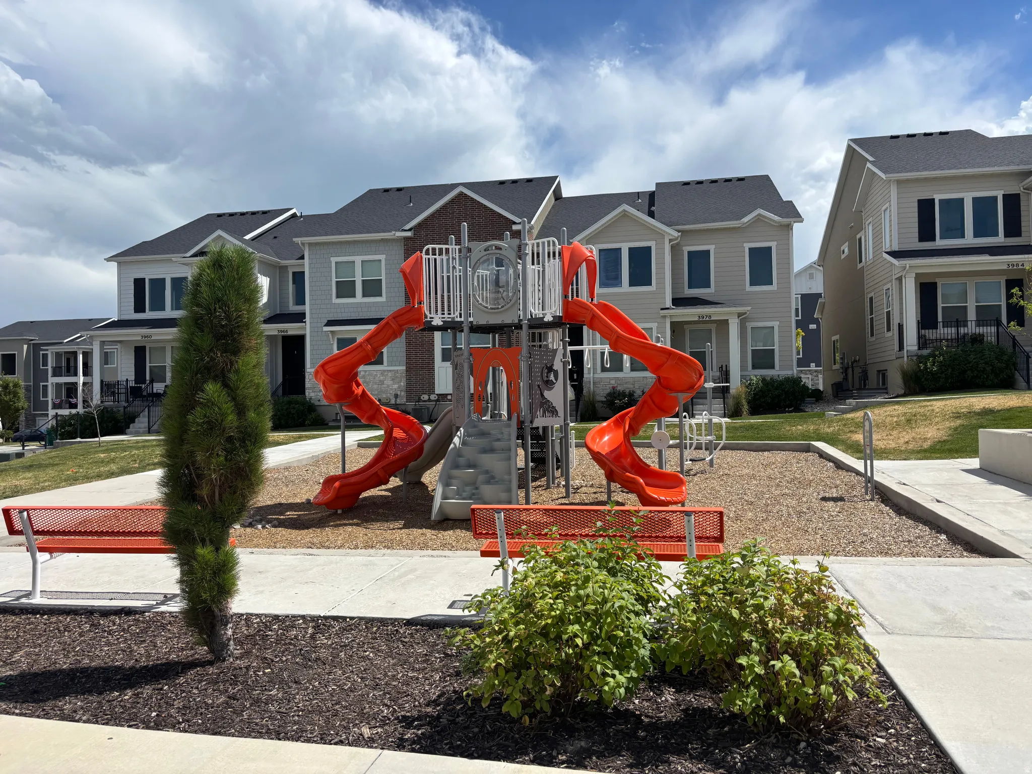 Community playground featuring orange slides and red benches, set against a backdrop of modern townhomes