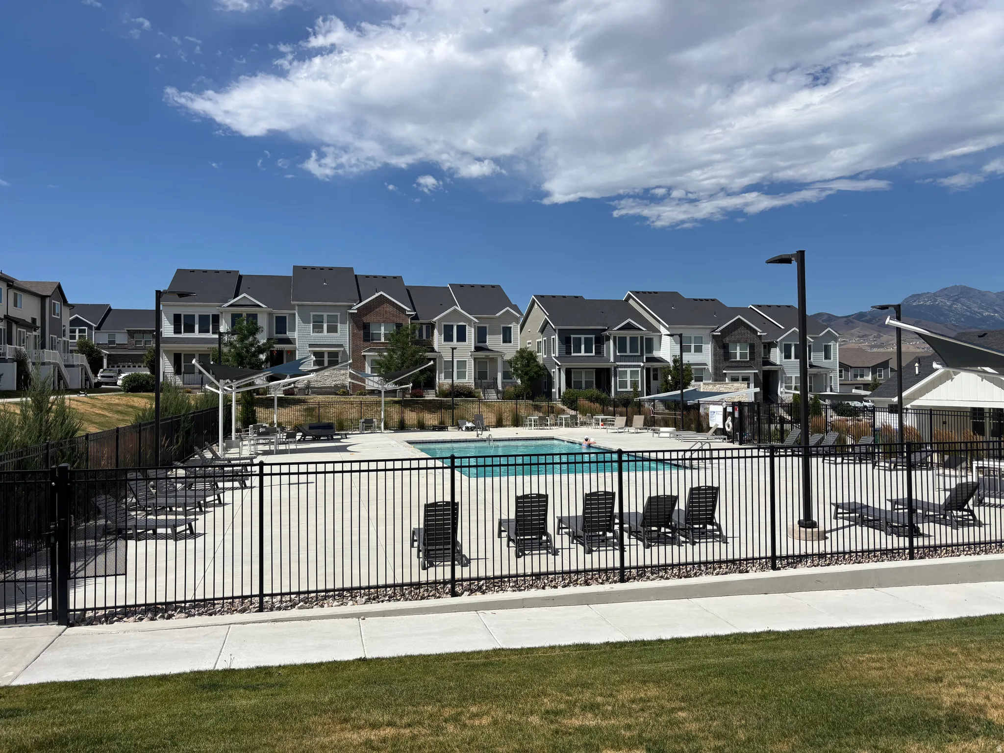 Community swimming pool with a surrounding concrete deck, black metal fencing, and multiple lounge chairs