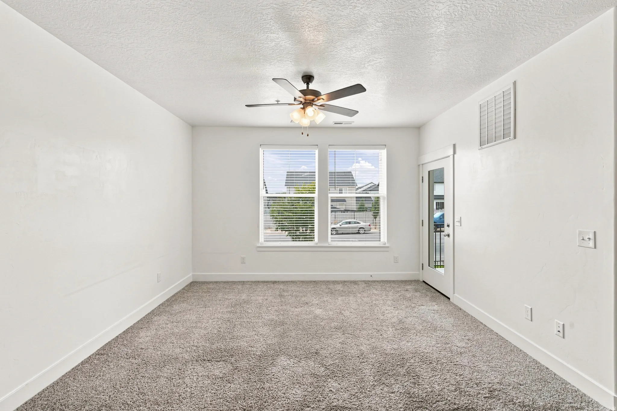 Spacious room featuring neutral carpeting, white walls, and a ceiling fan with integrated lighting