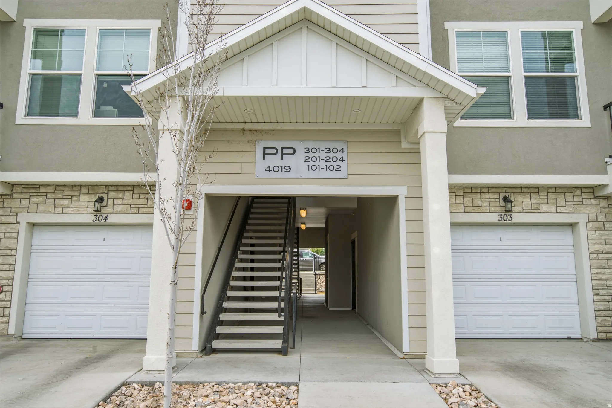 Multi-story residential facade featuring stone veneer accents, neutral siding, and prominent individual garage doors