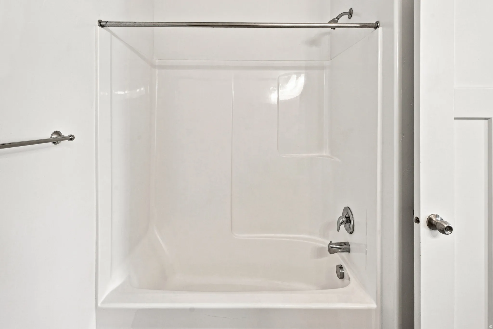 White fiberglass tub and shower combination with chrome fixtures and shower rod