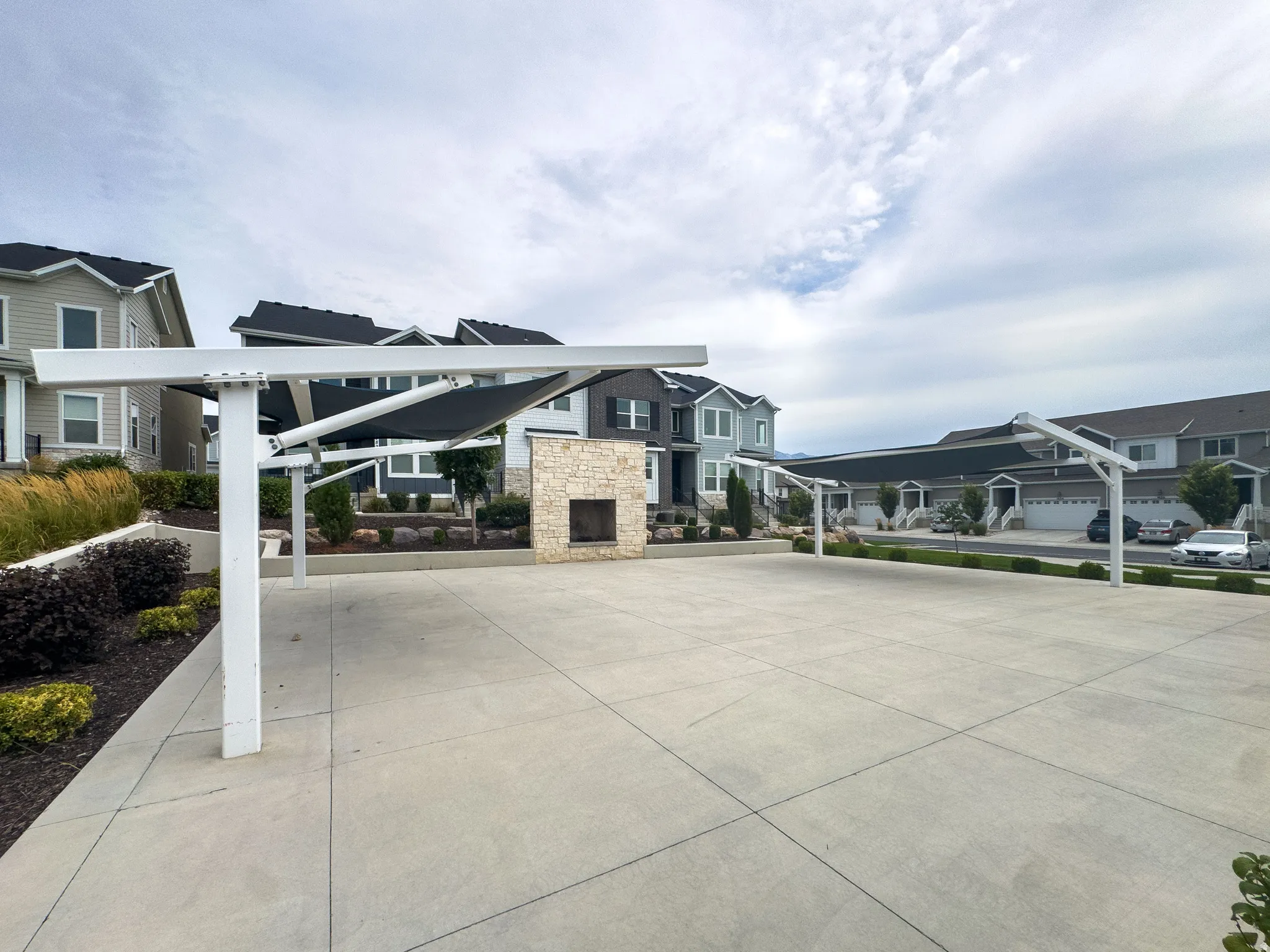 Expansive paved patio area featuring a stone-clad outdoor fireplace and a modern shade structure with a retractable canopy