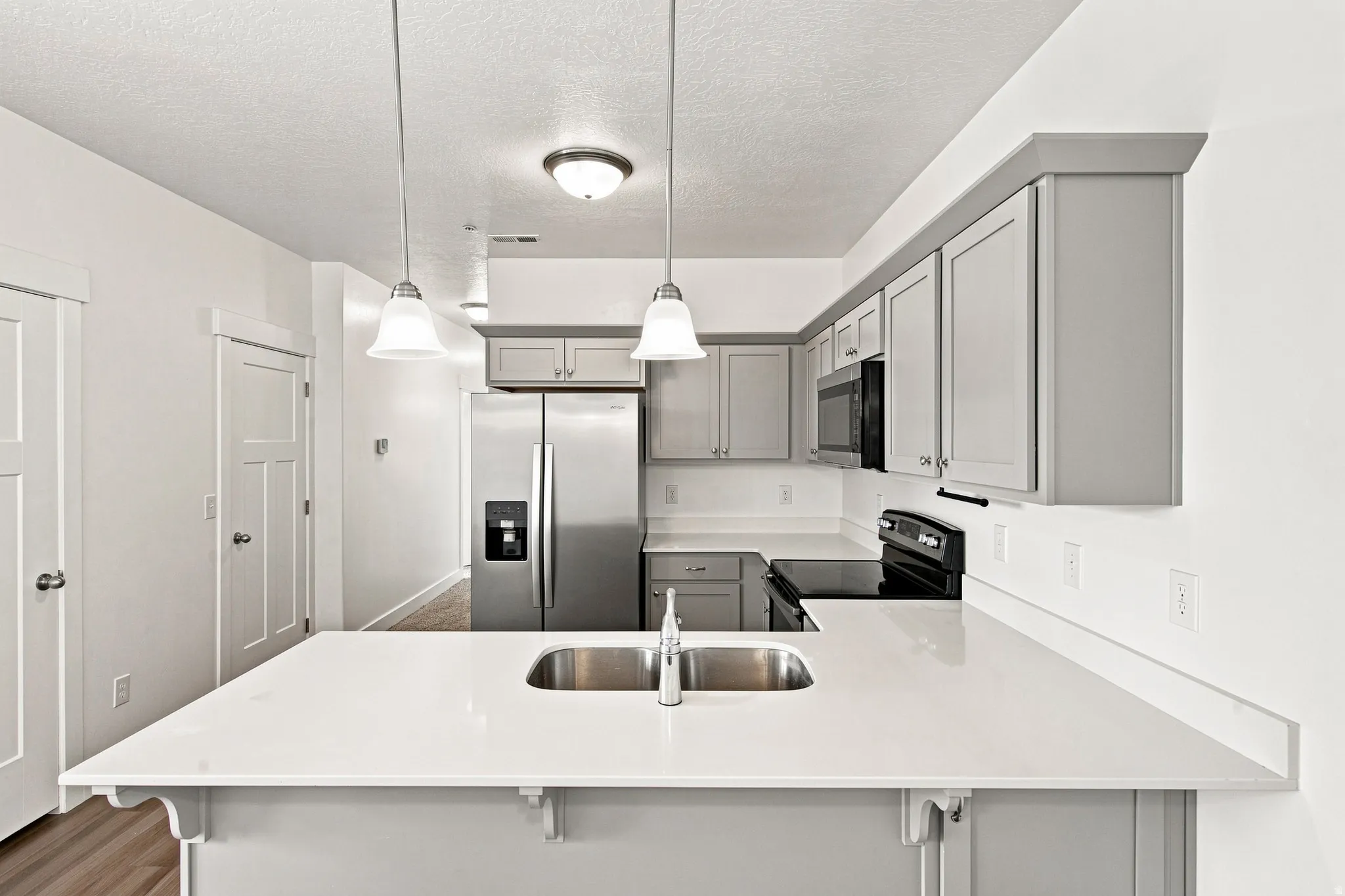 Kitchen featuring light gray cabinetry, stainless steel appliances, a white solid-surface island, and pendant lighting