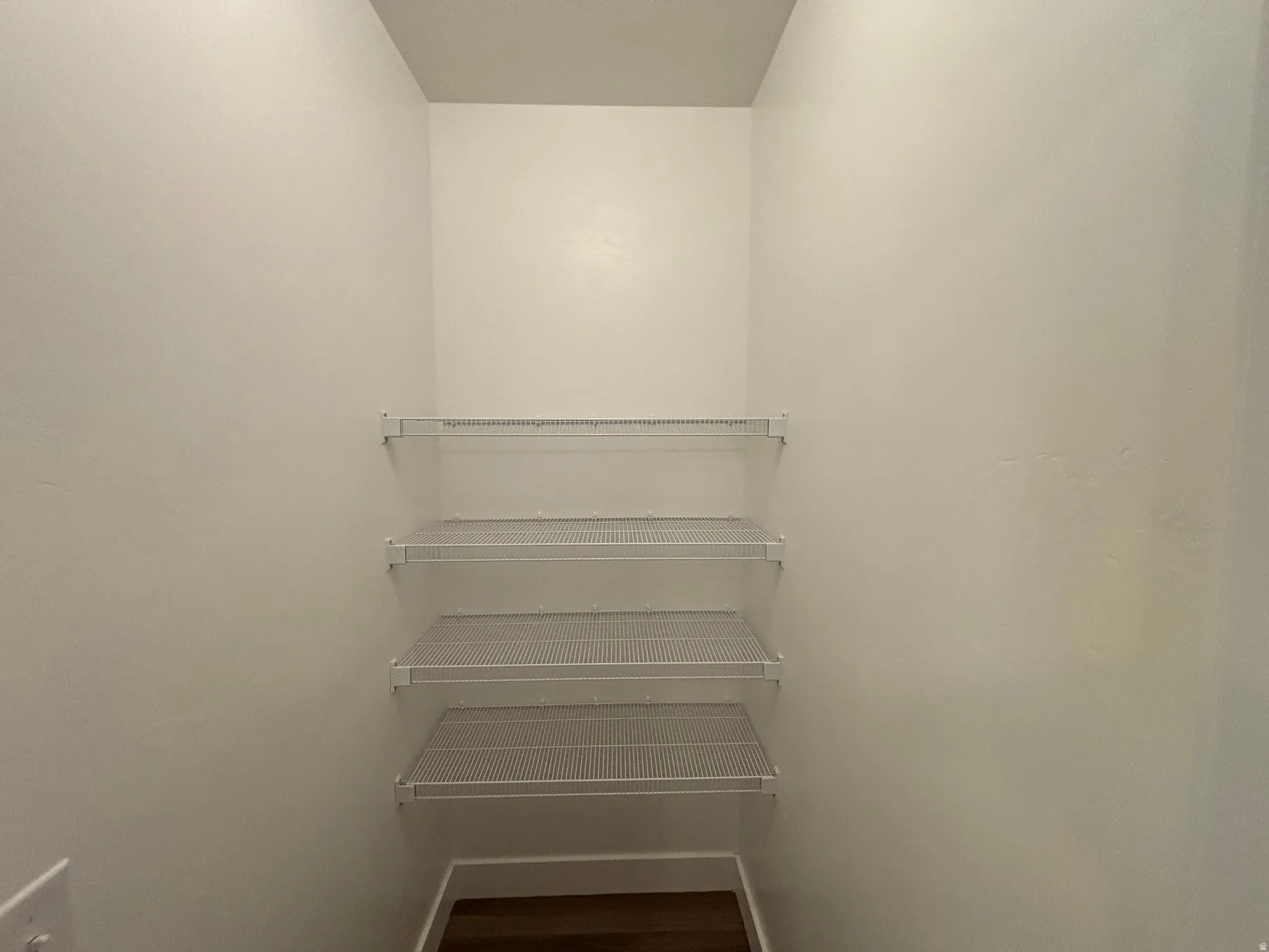 Recessed closet space with three white wire shelving units and wood-finish flooring