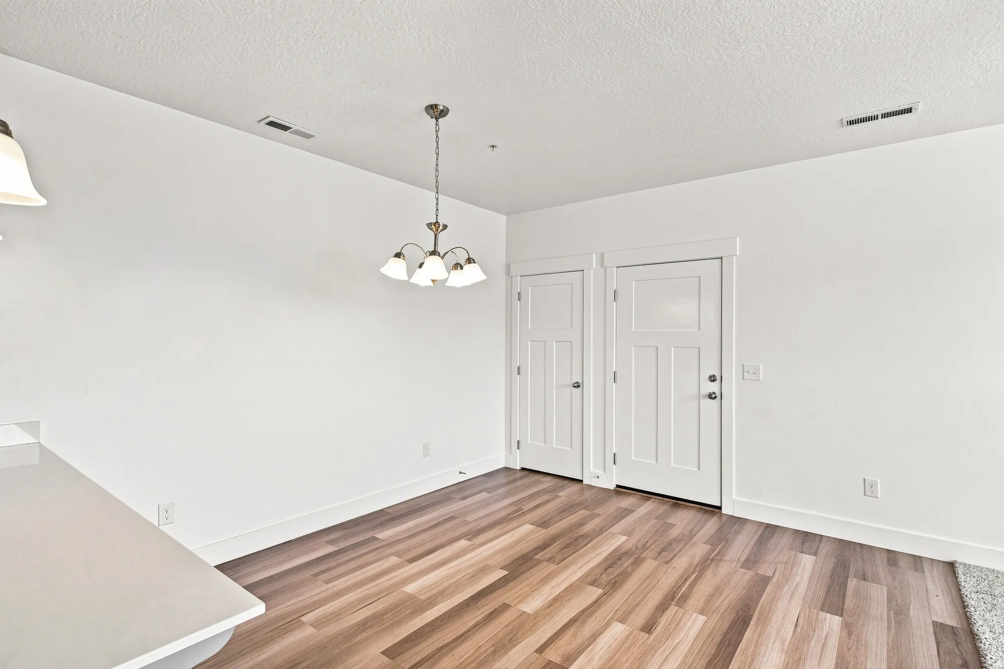 Spacious room featuring wood-finish flooring, crisp white walls, and a contemporary chandelier