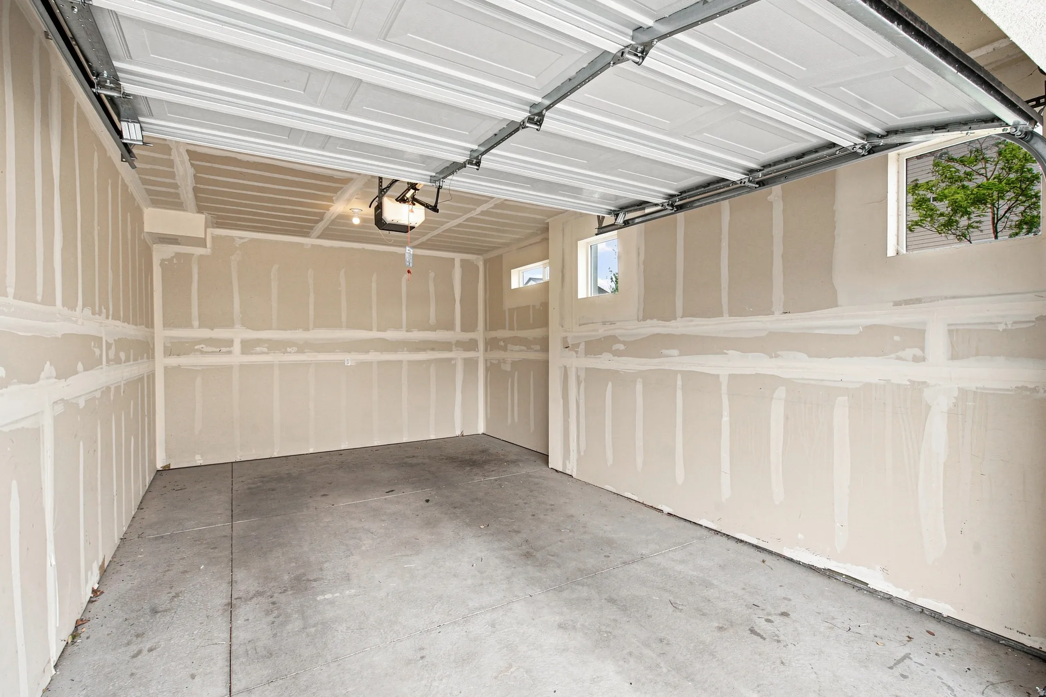 Unfinished garage space featuring a concrete floor, exposed drywall, and two high-set windows providing natural illumination