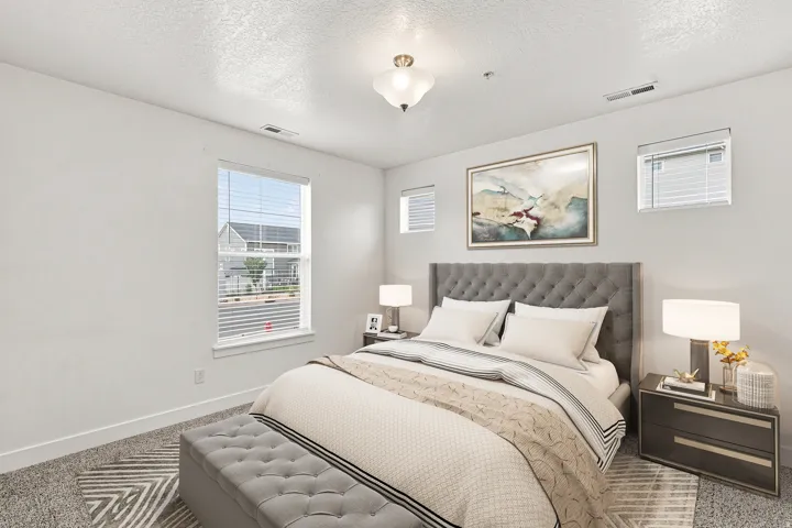 Carpeted room featuring a tufted headboard, multiple windows with blinds, a ceiling-mounted light fixture, and white baseboards