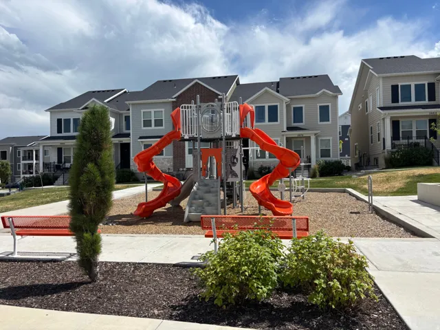 Community playground featuring orange slides and red benches, set against a backdrop of modern townhomes