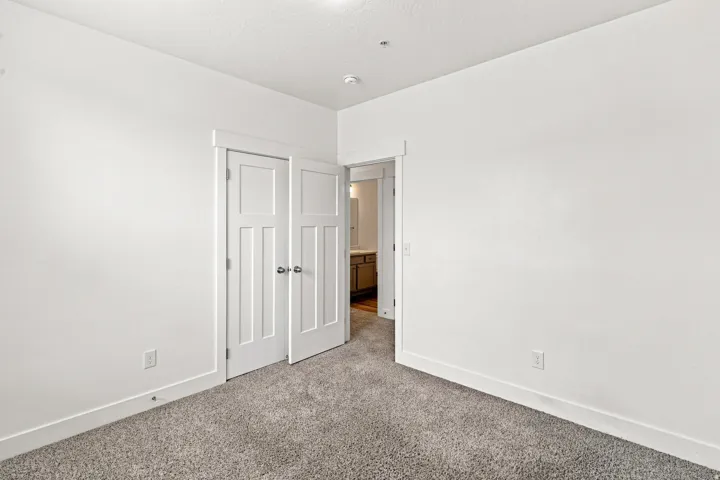 Carpeted room with white walls, featuring a pair of paneled doors with chrome hardware