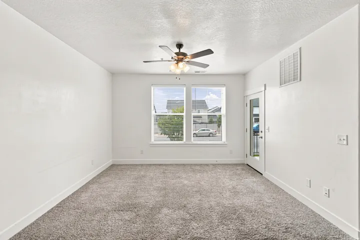 Spacious room featuring neutral carpeting, white walls, and a ceiling fan with integrated lighting
