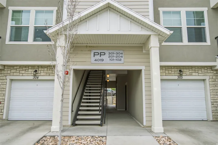 Multi-story residential facade featuring stone veneer accents, neutral siding, and prominent individual garage doors