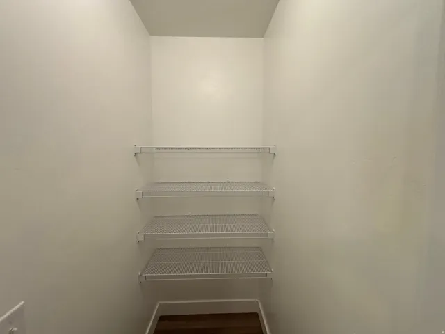 Recessed closet space with three white wire shelving units and wood-finish flooring