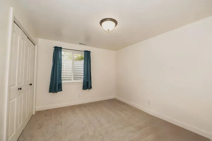 Neutral-toned interior room featuring light carpet flooring, white walls, and a window with a window well