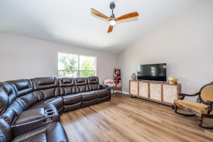 Living area featuring vaulted ceilings, wood-finish flooring, and a contemporary ceiling fan with integrated lighting
