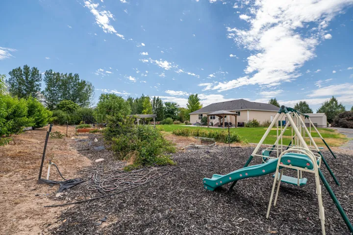Expansive backyard featuring a designated play area with a slide and swing set, a large grassy area, a covered patio, and mature trees