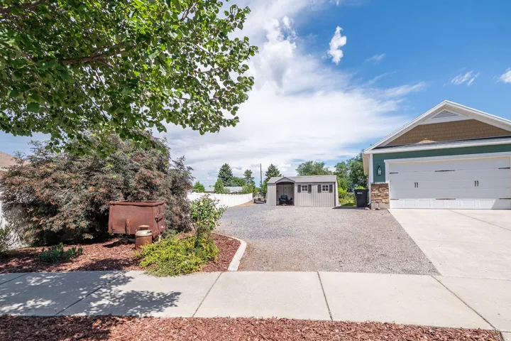 Front exterior showcasing a two-car garage with a concrete driveway, a separate gravel parking area, and two storage sheds
