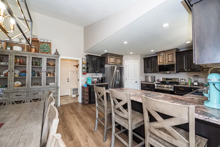 Spacious kitchen with a large island featuring a stone countertop, dark cabinetry, stainless steel appliances, and wood-finish flooring