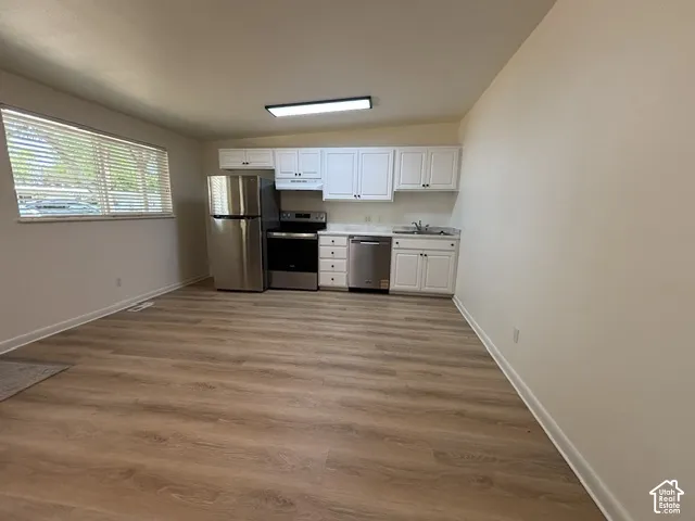 Open-concept kitchen featuring white cabinetry, stainless steel appliances, and wood-finish flooring