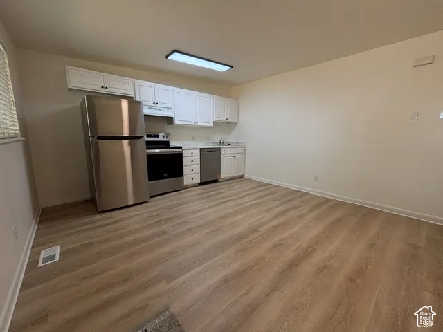 Kitchenette with white cabinetry, stainless steel appliances, light countertops, and wood-finish flooring