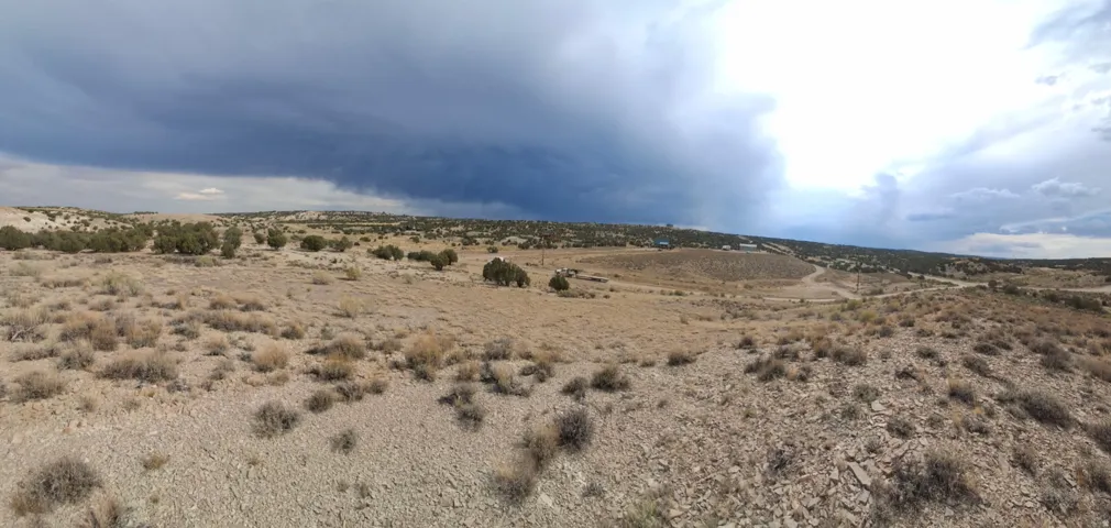 Expansive high desert terrain featuring scattered native brush and distant structures