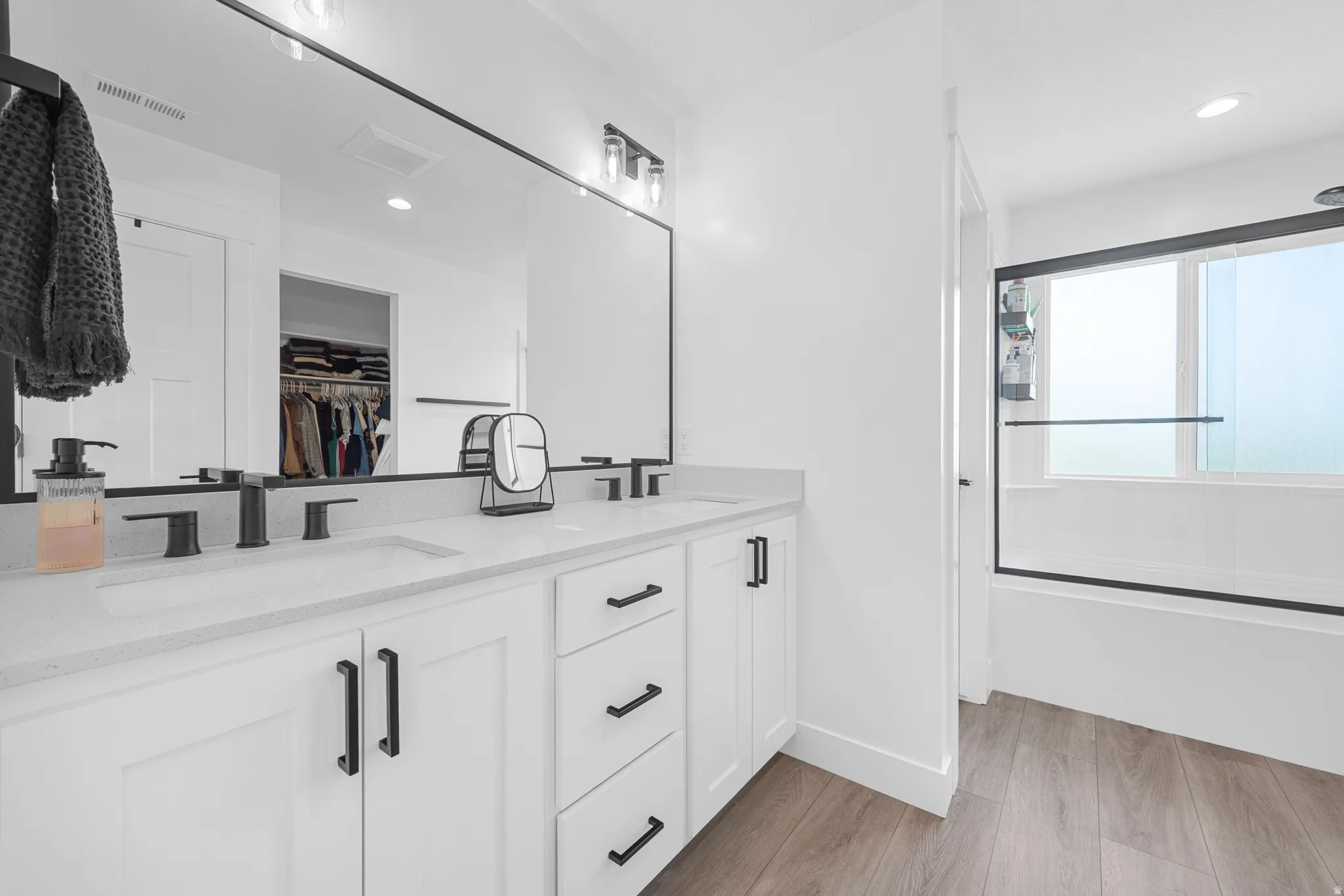 Dual vanity with white cabinetry, matte black hardware, and an expansive mirror