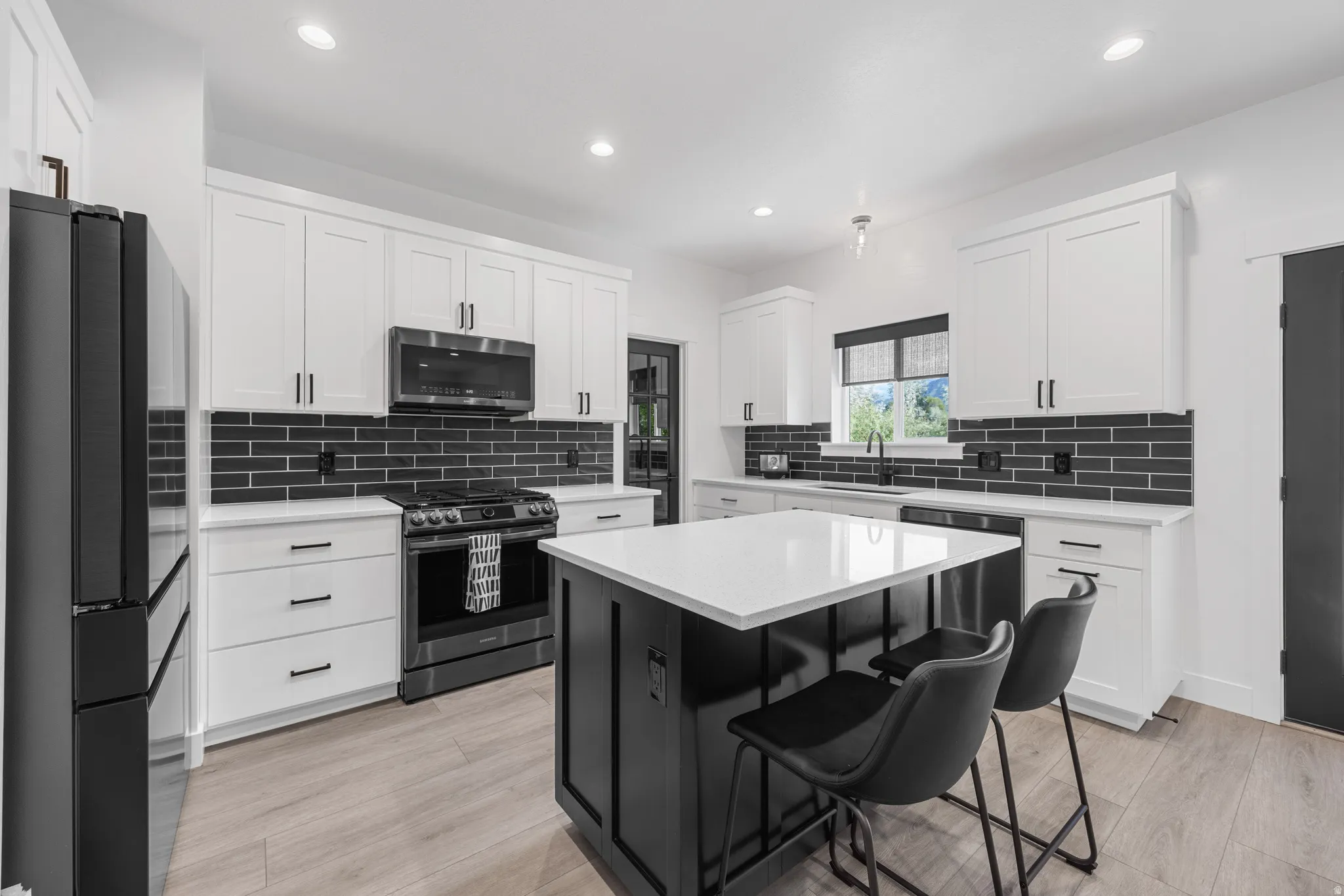 Kitchen featuring white shaker cabinetry, black subway tile backsplash, stainless steel appliances, a center island with seating, and wood-finish flooring