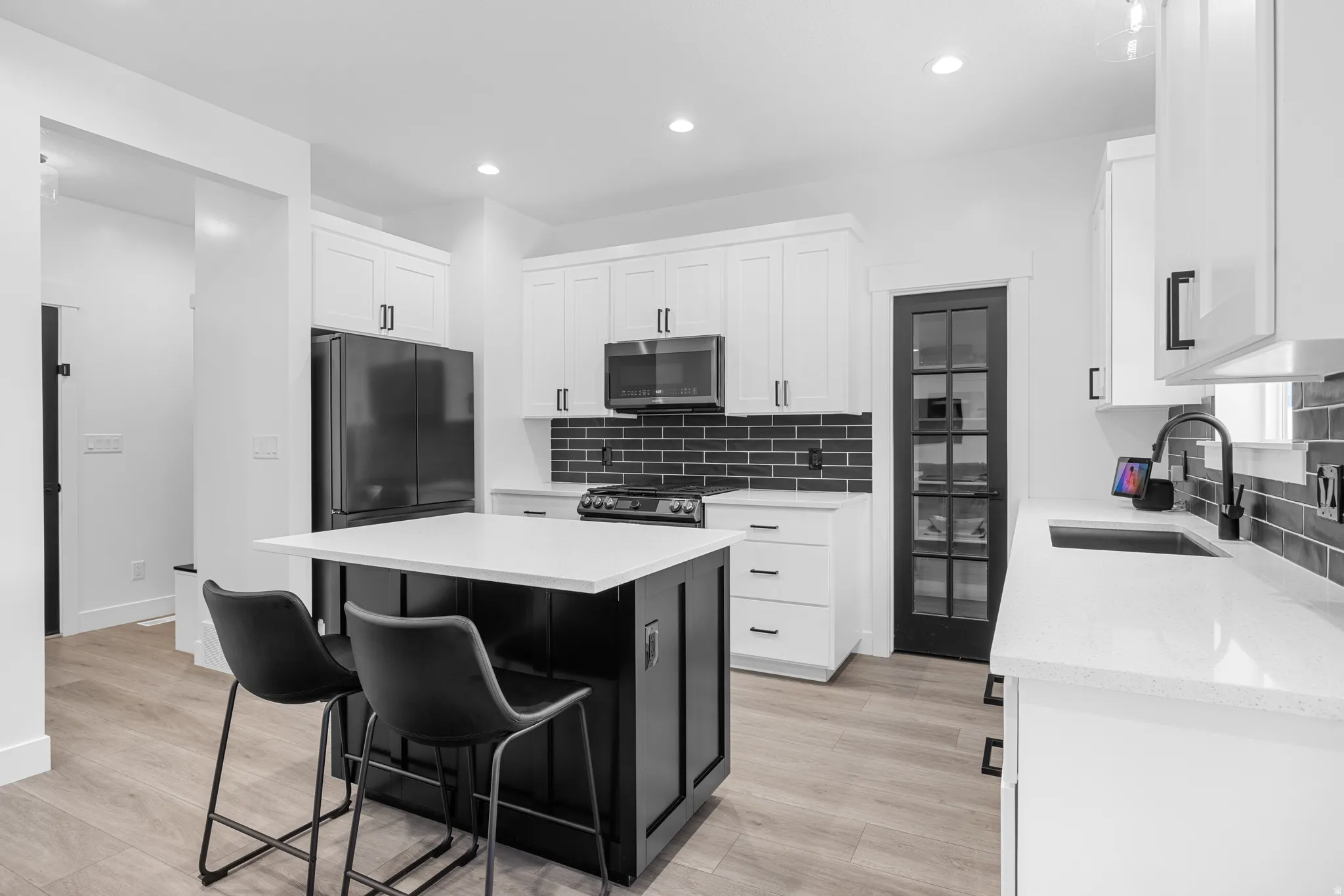 Modern kitchen featuring white cabinetry, a large center island with a white countertop, black subway tile backsplash, and wood-finish flooring