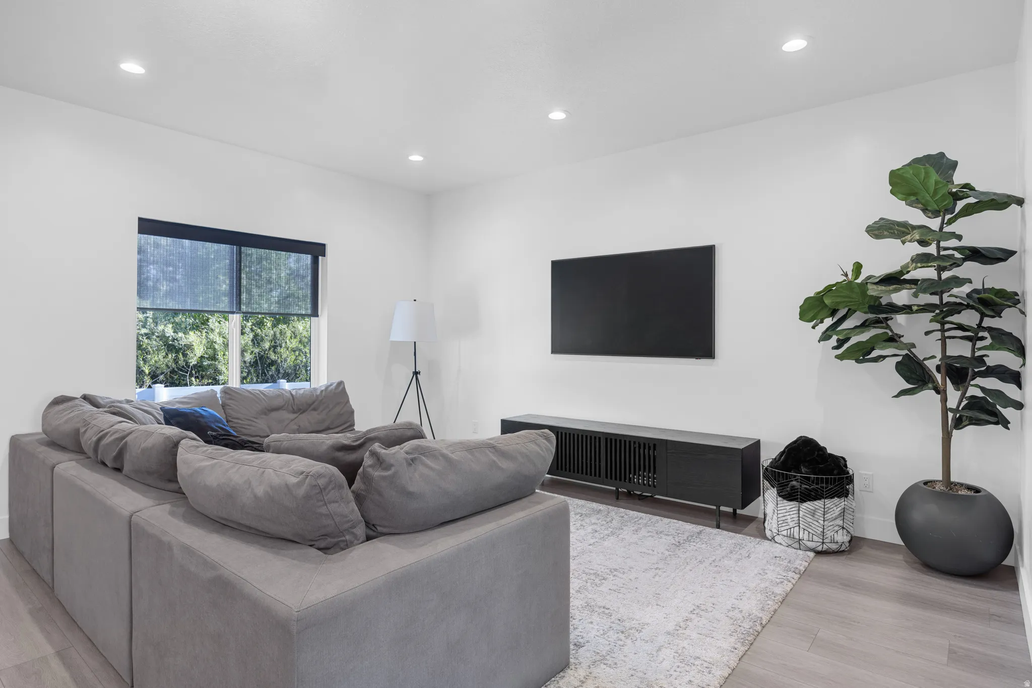 Bright living area featuring recessed lighting, a large window with roller shades, and light wood-finish flooring