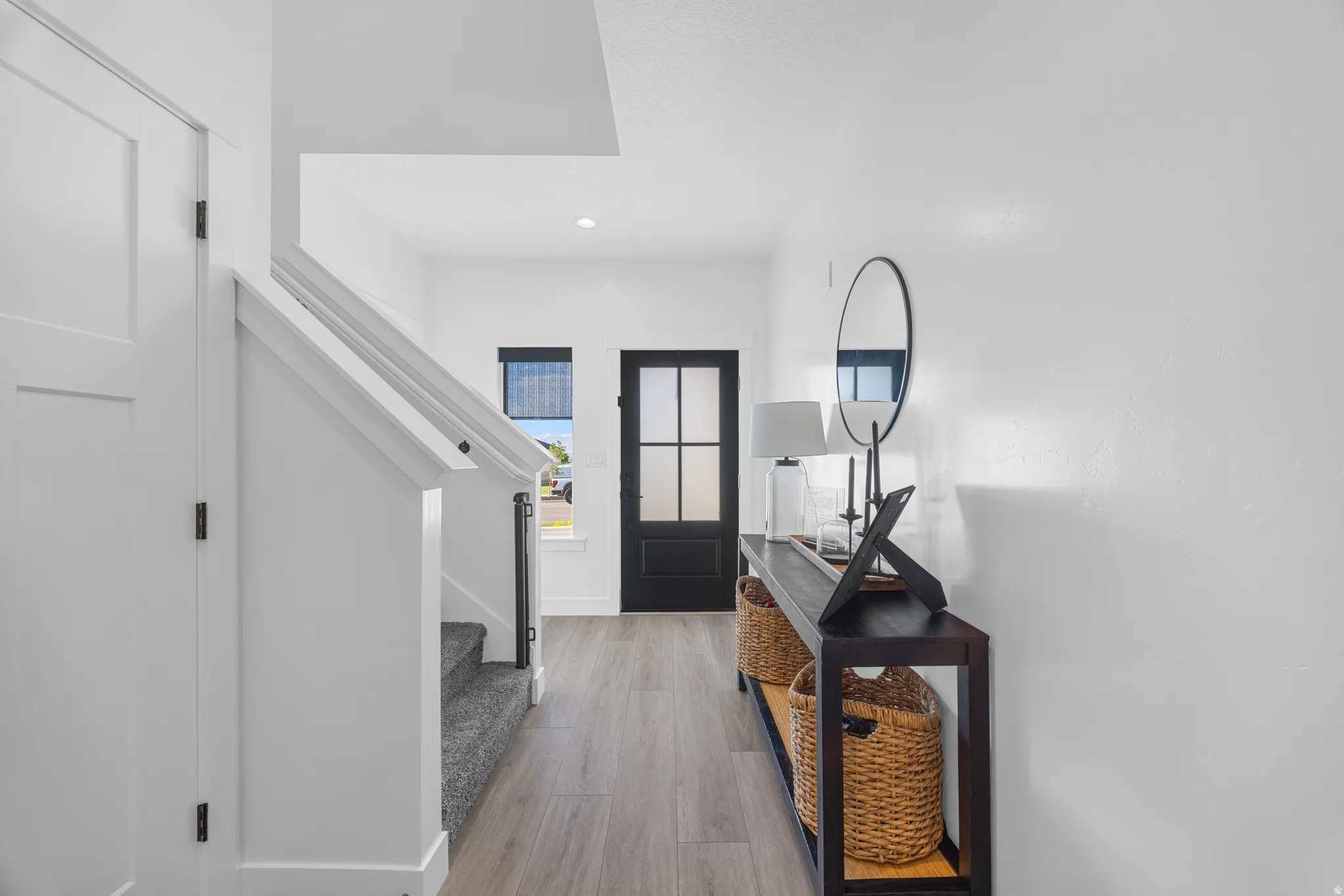 Entryway featuring light wood-finish flooring, a contemporary black paneled door with frosted glass, and a staircase with white risers and carpeted treads