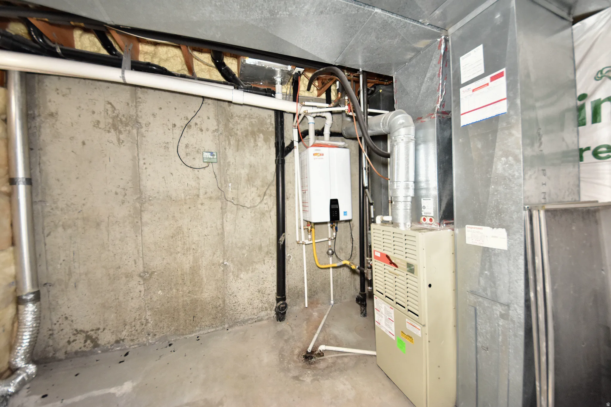 Basement utility area featuring a wall-mounted tankless water heater, gas furnace, and extensive ductwork