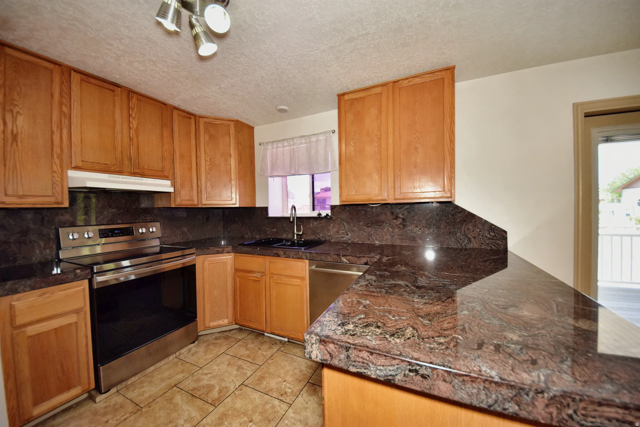 Kitchen featuring wood cabinetry, dark patterned countertops, a stainless steel electric range, and a stainless steel dishwasher
