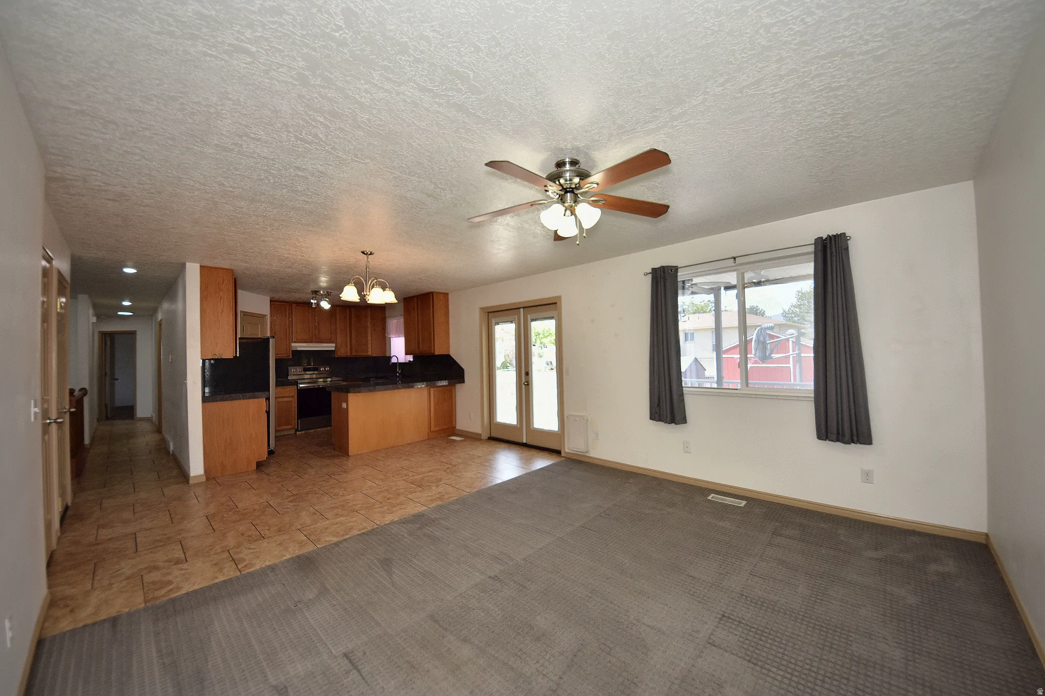Open-concept living space featuring a ceiling fan, a kitchen with wood cabinetry and dark countertops, and a dining area with pendant lighting