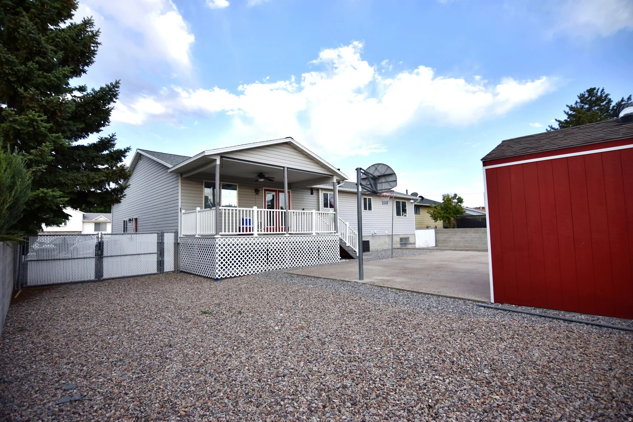 Gravel yard area featuring a red utility shed, paved court, and a covered deck with white railing