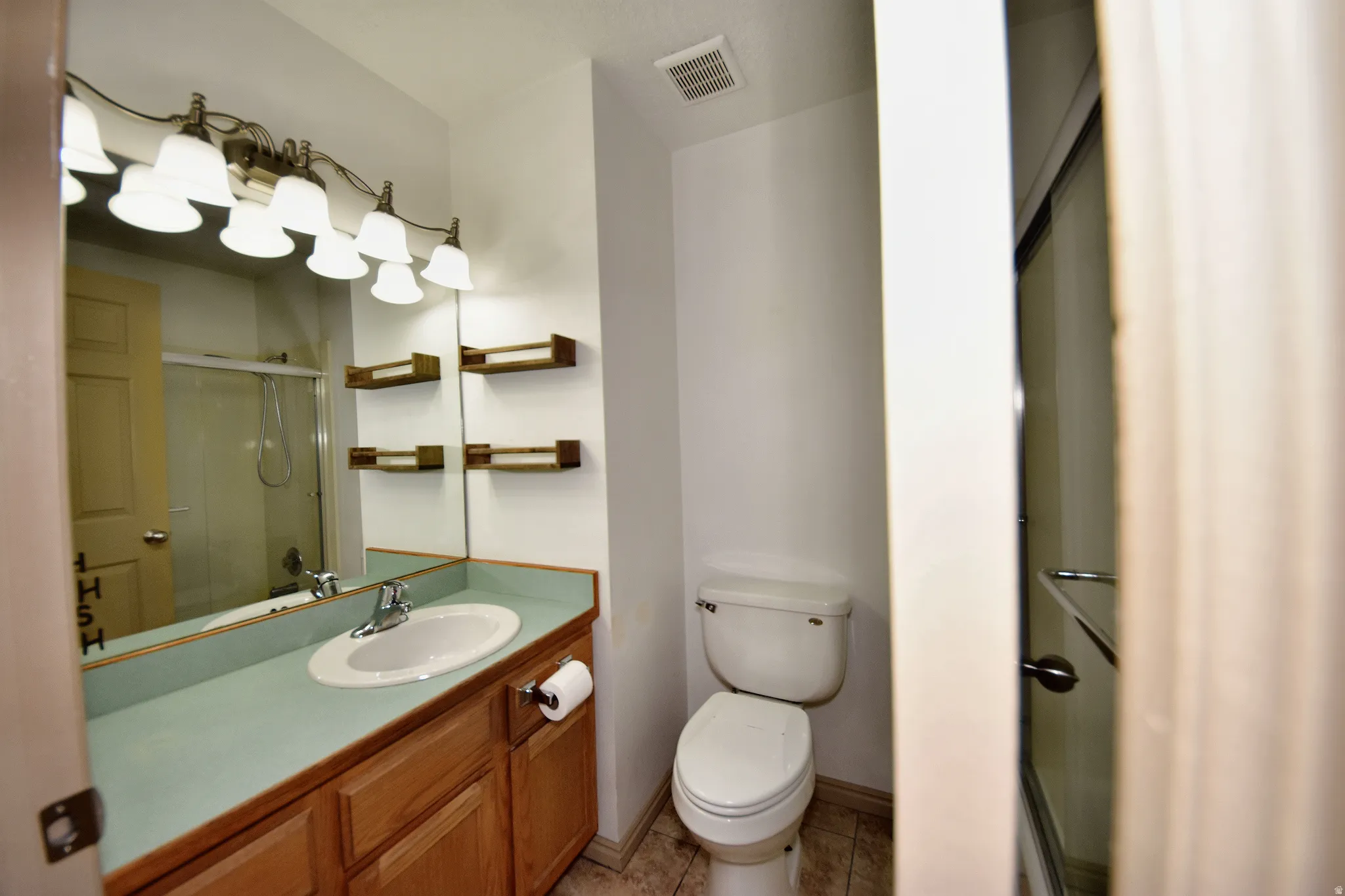 Bathroom with a single vanity, light wood cabinetry, a light blue countertop, and a large mirror