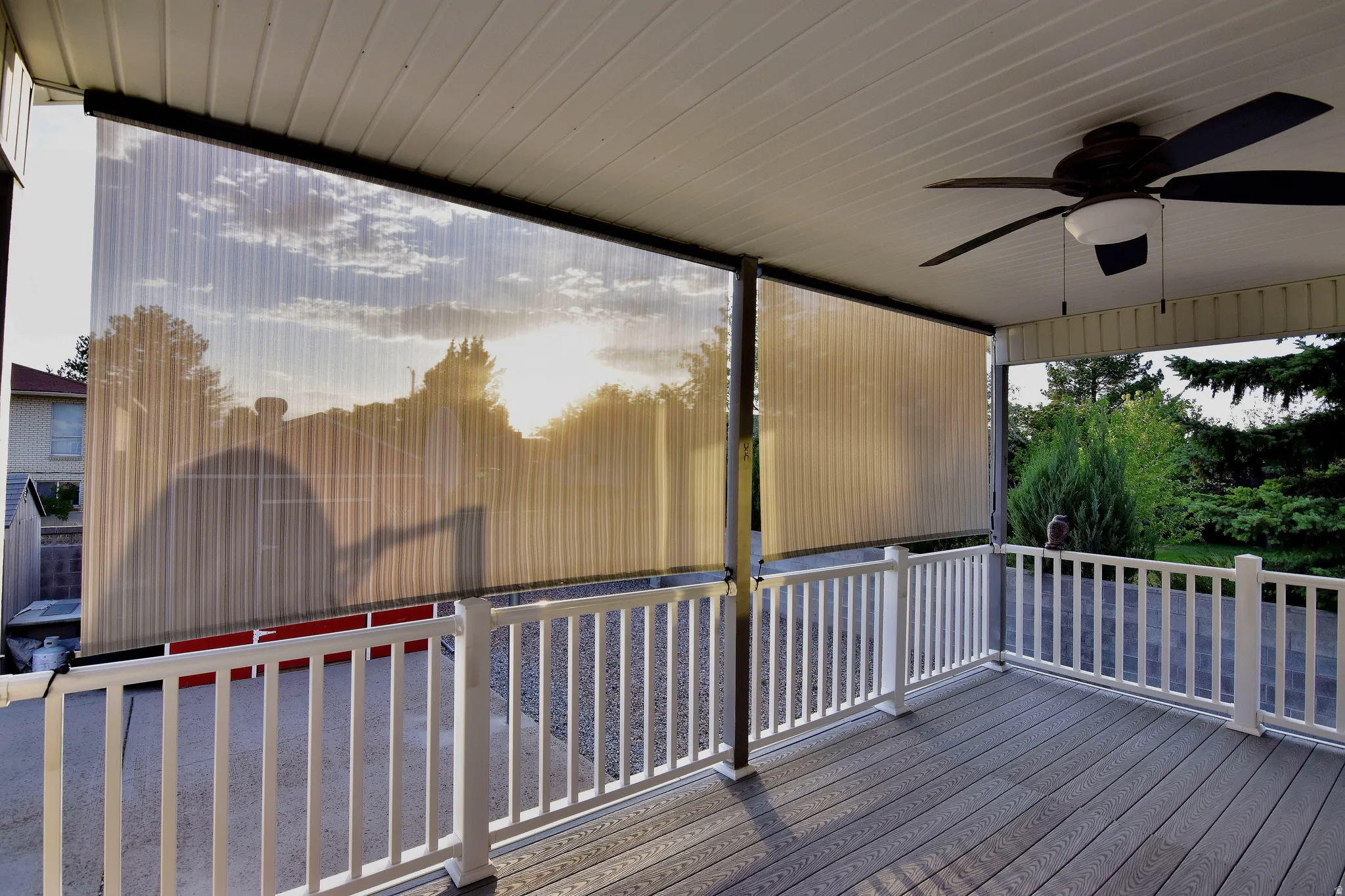 Covered porch with wood-finish decking, white railing, and ceiling fan with integrated lighting