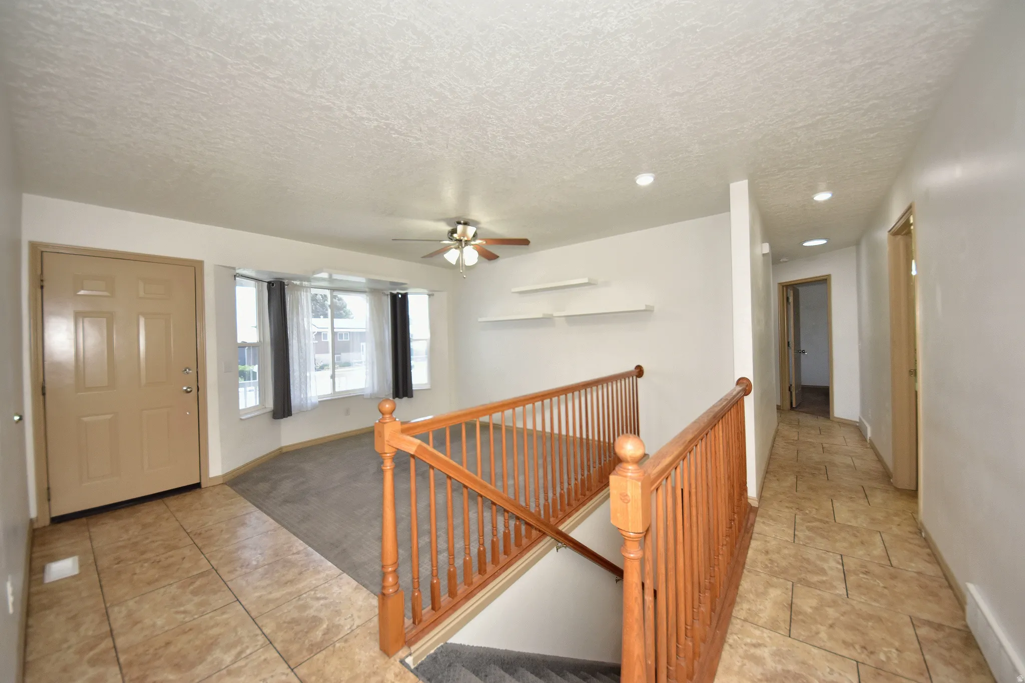 Inviting entry foyer featuring ceramic tile flooring, a staircase with wood railings, and a living area with a bay window