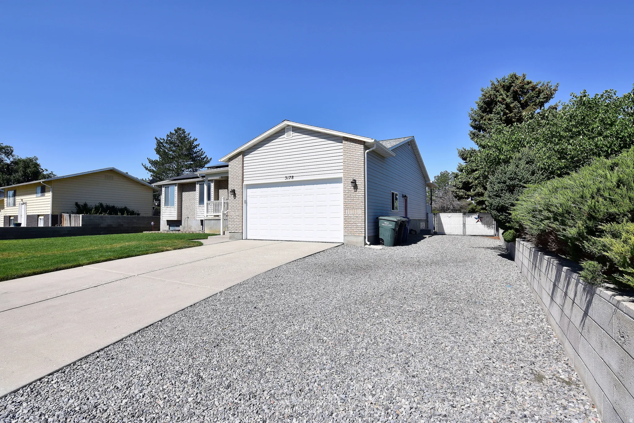 Split-level residence featuring a two-car garage with a white overhead door, complemented by a concrete driveway and an additional gravel parking area