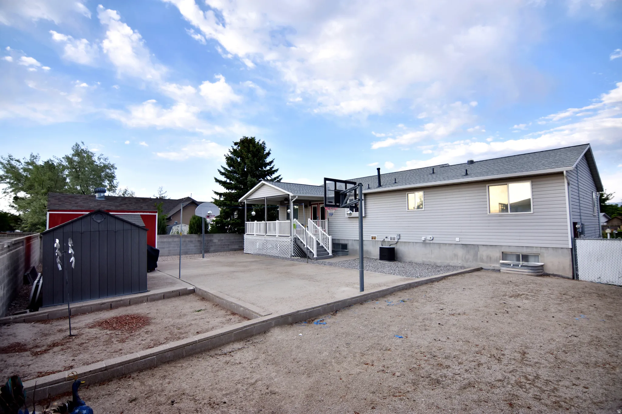 Expansive backyard featuring a concrete patio, covered porch with white railings, and a detached storage shed